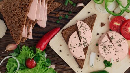 sandwich of rye bread with boiled sausage and vegetables on a rustic wooden backgroundの写真素材