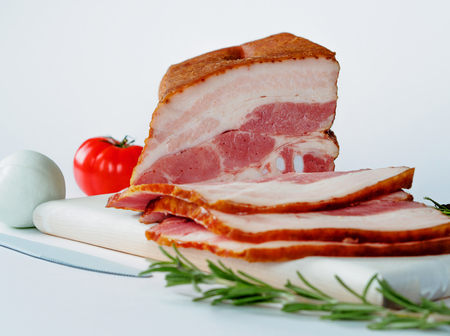 Smoked bacon on white cutting board with white colored tomatoes and knife on white backgroundの写真素材