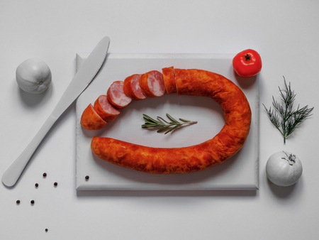 Smoked sausage on white cutting board with white colored tomatoes and knife on white backgroundの写真素材