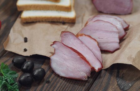 Piece of smoked Ham with some fresh herbs and bread on wooden cutting board on wooden backgroundの写真素材
