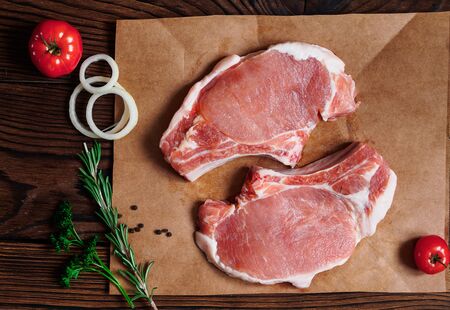 Fresh raw pork steaks on a craft paper with herbs on wooden backgroundの写真素材