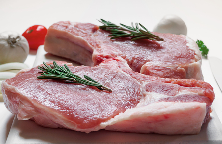 Raw ribeye pork steaks on white painted cutting board with white colored tomatoes and knife on white backgroundの写真素材