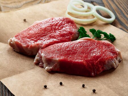 Fresh raw pork steaks on a craft paper with herbs on wooden backgroundの写真素材