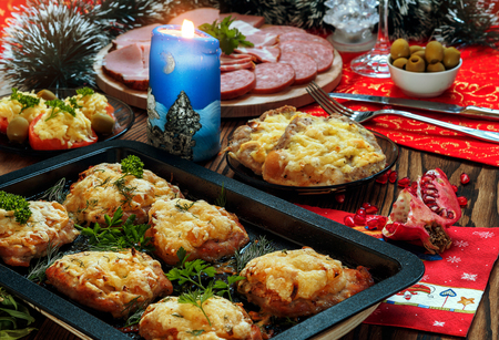 Christmas baked chops with cheese and cold cuts platter, served on the old wooden table with a red tableclothの写真素材