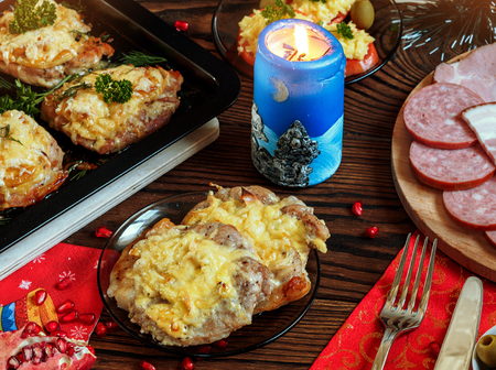 Christmas baked chops with cheese and cold cuts platter, served on the old wooden table with a red tableclothの写真素材