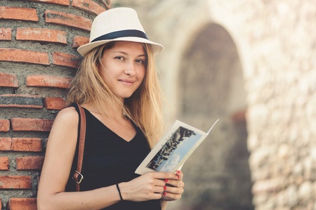 Young tourist woman in black dress standing with booklet on the brick wall background in old town square in Georgiaの写真素材