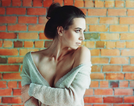 Stylish brunette woman in white sweater posing near red brick wallの写真素材