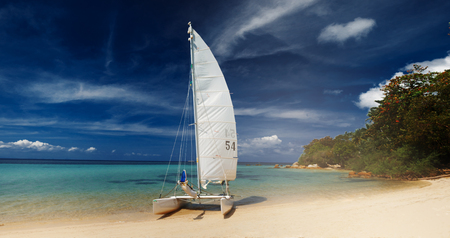 Sail boat, catamaran, on tropical beach with blue water backgroundの写真素材