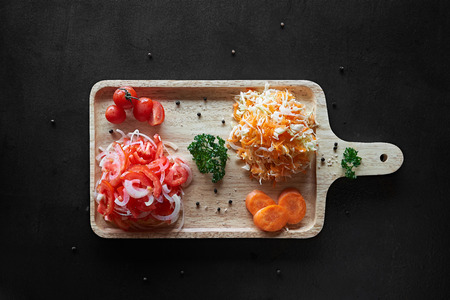 Healthy vegetable salad of fresh tomato, carrot, onion on cutting board on black tableの写真素材
