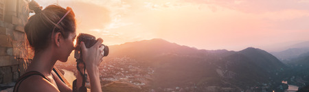 Female photographer, taking pictures of mountain landscape at sunset, long panoramicの写真素材
