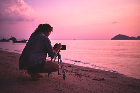 Woman photographer, taking pictures of landscape at sunsetの写真素材