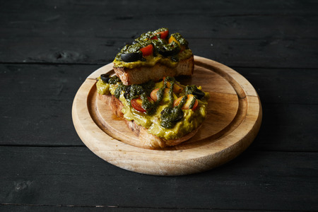 Fresh avocado toast with spices on wooden cut board on dark background, top viewの写真素材