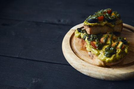 Fresh avocado toast with spices on wooden cut board on dark background, top viewの写真素材