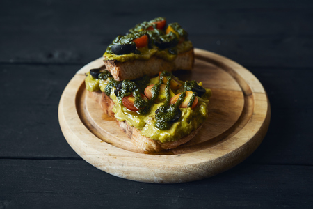 Fresh avocado toast with spices on wooden cut board on dark background, top viewの写真素材