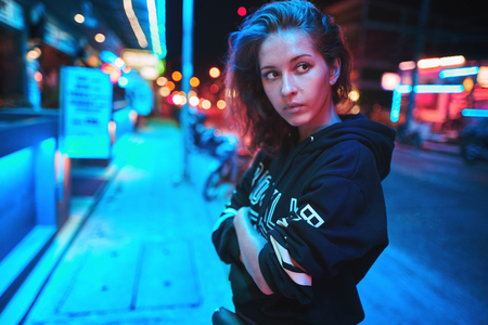 Neon close up portrait of young woman wear hoodie. night city street shotの写真素材