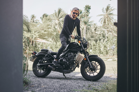 Handsome biker man in black wear sit on classic style cafe racer motorcycle. custom made motorcycleの写真素材