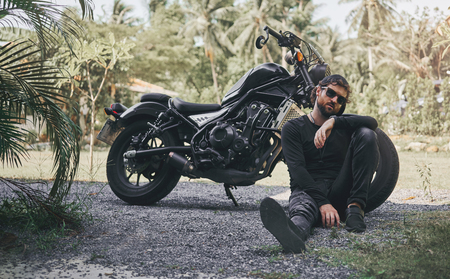 Handsome biker man in black wear sit near classic style cafe racer motorcycle. custom made motorcycle