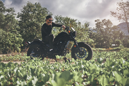 Handsome biker man in black wear sit on classic style cafe racer motorcycle. custom made motorcycleの写真素材
