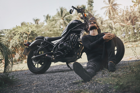 Handsome biker man in black wear sit near classic style cafe racer motorcycle. custom made motorcycleの写真素材