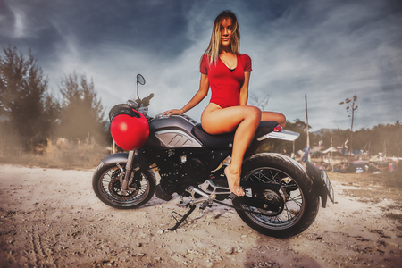 Outdoor lifestyle portrait of young sexy woman in red swimsuit sitting on a vintage custom motorcycleの写真素材