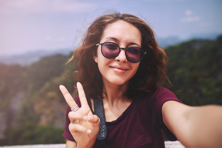 Portrait of a smiling young girl making selfie photo in the mountainsの写真素材