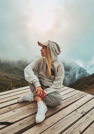 a girl in a grey hoodie sitting on a viewpoint and watching sunsetの写真素材
