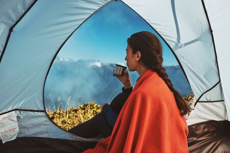 young hiker drinks tea from flask in tent in the morningの写真素材
