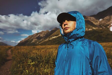 A young hiker in a blue jacket standing and looking up in the mountainsの写真素材