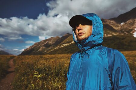 A young hiker in a blue jacket standing and looking up in the mountainsの写真素材