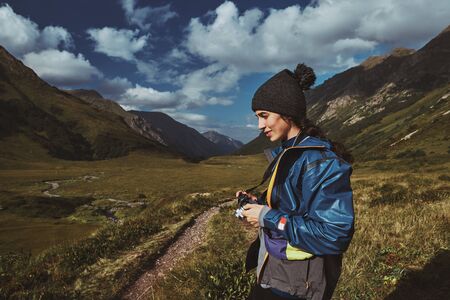 A young woman hiker in a blue jacket standing with her camera near footpath in the mountainsの写真素材