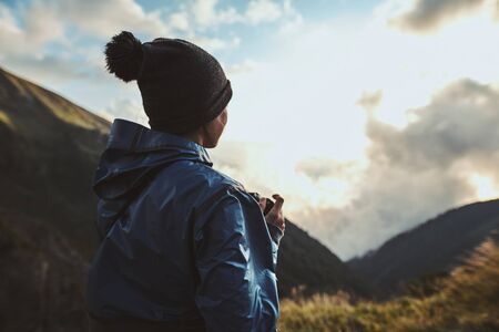 A young woman hiker in a blue jacket standing with her camera near footpath in the mountainsの写真素材