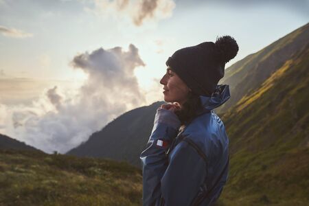 A young woman hiker in a blue jacket standing in the mountainsの写真素材