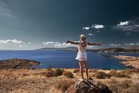 young woman traveler standing on a rock and putting her arms up, Bodrum bay on backgroundの写真素材