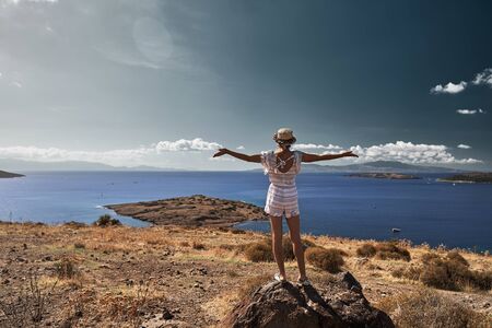 young woman traveler standing on a rock and putting her arms up, Bodrum bay on backgroundの写真素材