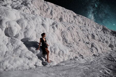 Surrealistic photo of a young beautiful girl in a black dress standing by the Pamukkale natural pool with space in the backgroundの写真素材
