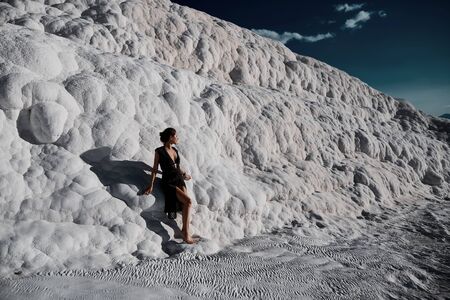 Young beautiful girl in black dress standing at natural pool Pamukkaleの写真素材