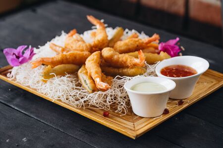 Shrimps in tempura on the crispy noodle with sauces on black wooden backround. Top view