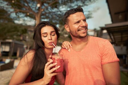 Young happy couple with drinks relaxing on the beachの写真素材