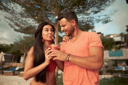 Young happy couple with drinks relaxing on the beachの写真素材