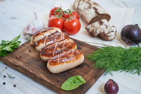 grilled sausages with tomatoes and herbs on the board on white tableの写真素材