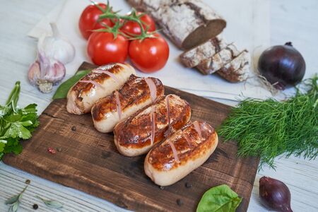 grilled sausages with tomatoes and herbs on the board on white tableの写真素材