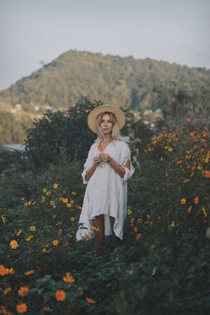 The blonde in a linen dress walks among herbs and wildflowers on a meadow in the mountains