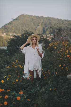 The blonde in a linen dress walks among herbs and wildflowers on a meadow in the mountainsの写真素材