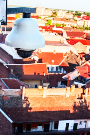High tech overhead security camera at a tall building oversees City area の写真素材