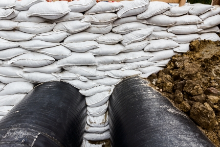 White sandbag bags are full with sand in wall formation to hold the Earth near traffic road  Industrially isolated pipes for distance heating passes under the road の写真素材