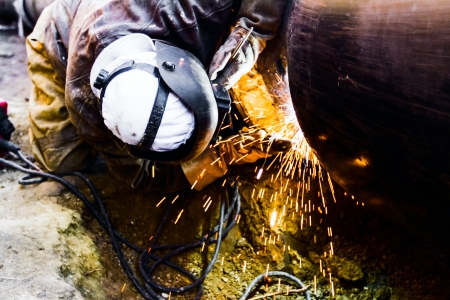 Welder working on a pipeline in construction site wearing overall and safety equipment