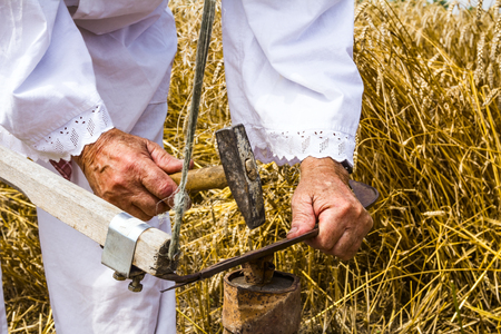 Man is sharpening a scythe which is used to mow grain の写真素材
