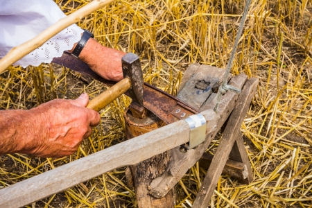 Man is sharpening a scythe which is used to mow grain の写真素材