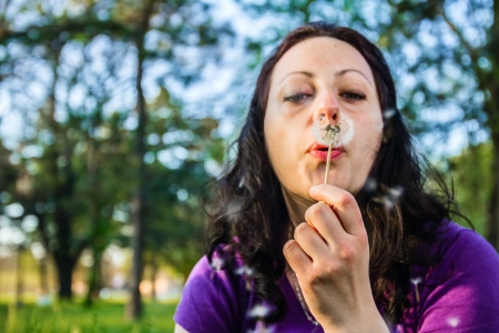 Curly  young woman blowing a dandelion in parkの写真素材