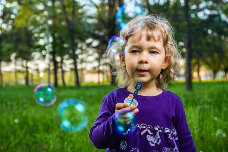 Beautiful little girl blowing soap bubbles in park.